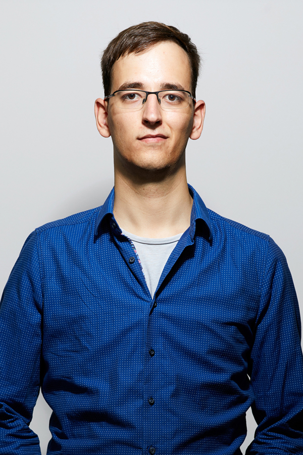 Employee photo by Alexander Hohlfeld. A man in a blue shirt stands in front of a white wall