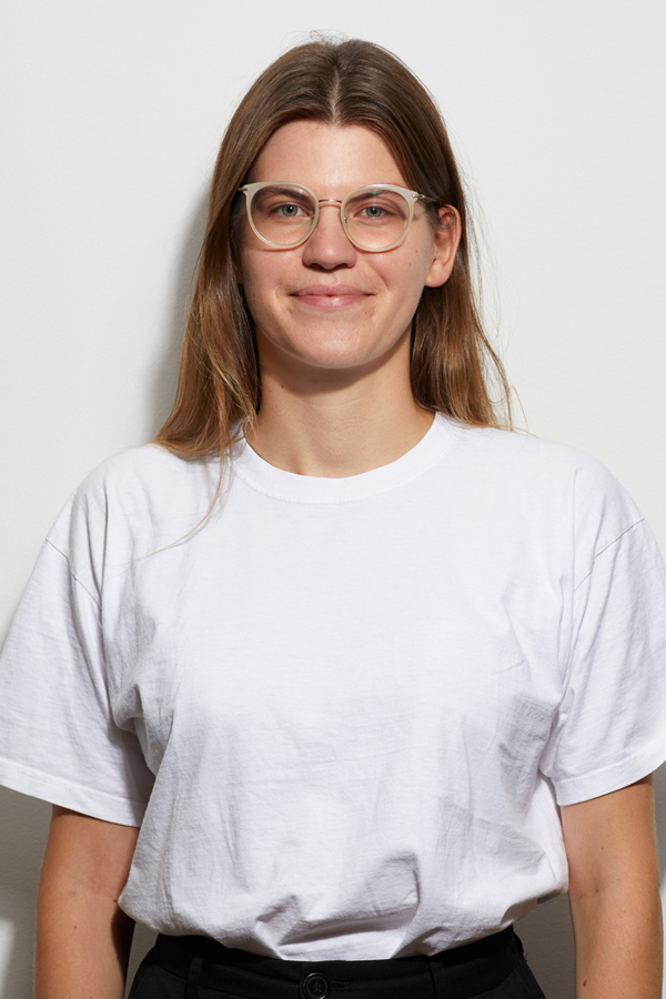 Staff photo of Hannah Aeterna Borne. She wears a white T-shirt and stands in front of a white wall.