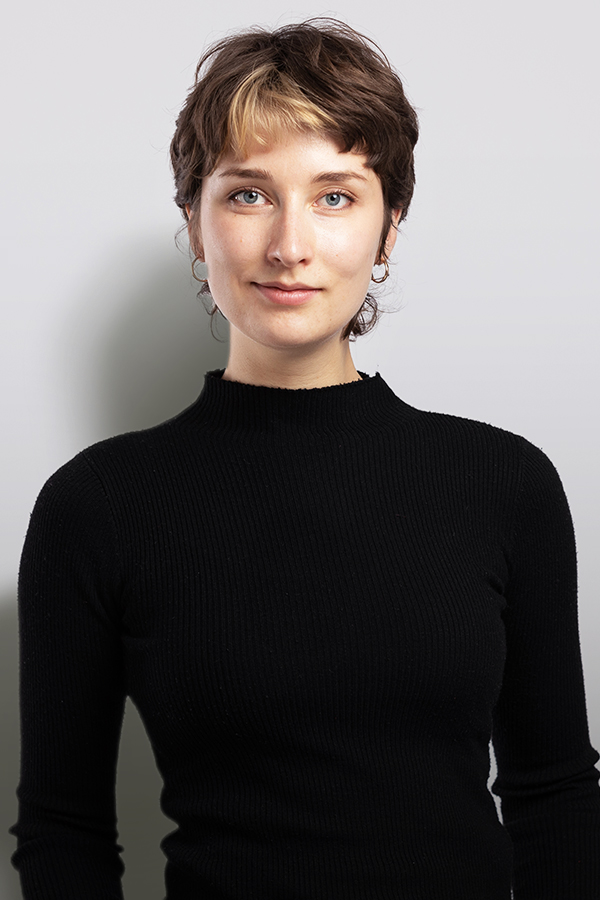 Staff photo of Lilly Goll. She is wearing a black sweater and standing in front of a white wall.