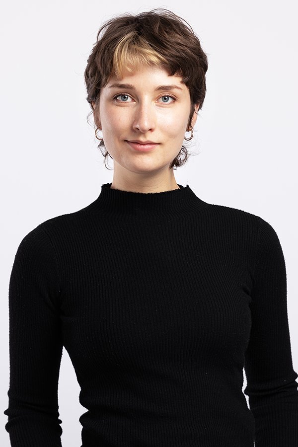 Staff photo of Lilly Goll. She is wearing a black sweater and standing in front of a white wall.