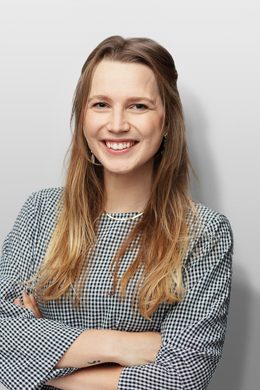 Staff photo of Lisa Soder. She is wearing a black and white checked shirt and stands in front of a white wall.