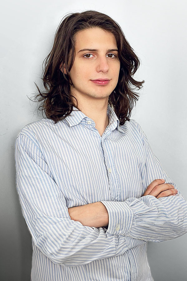 Employee photo of Ruggero Marino Lazzaroni. He is wearing a blue-white striped shirt and standing in front of a white wall.